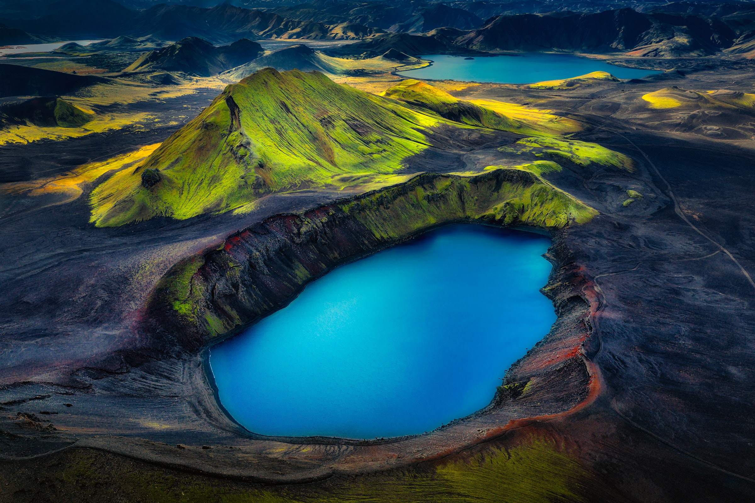 Elemental - aerial view of a turquoise crater lake and green volcanic ridges in Iceland's Highlands - SLG Masterworks