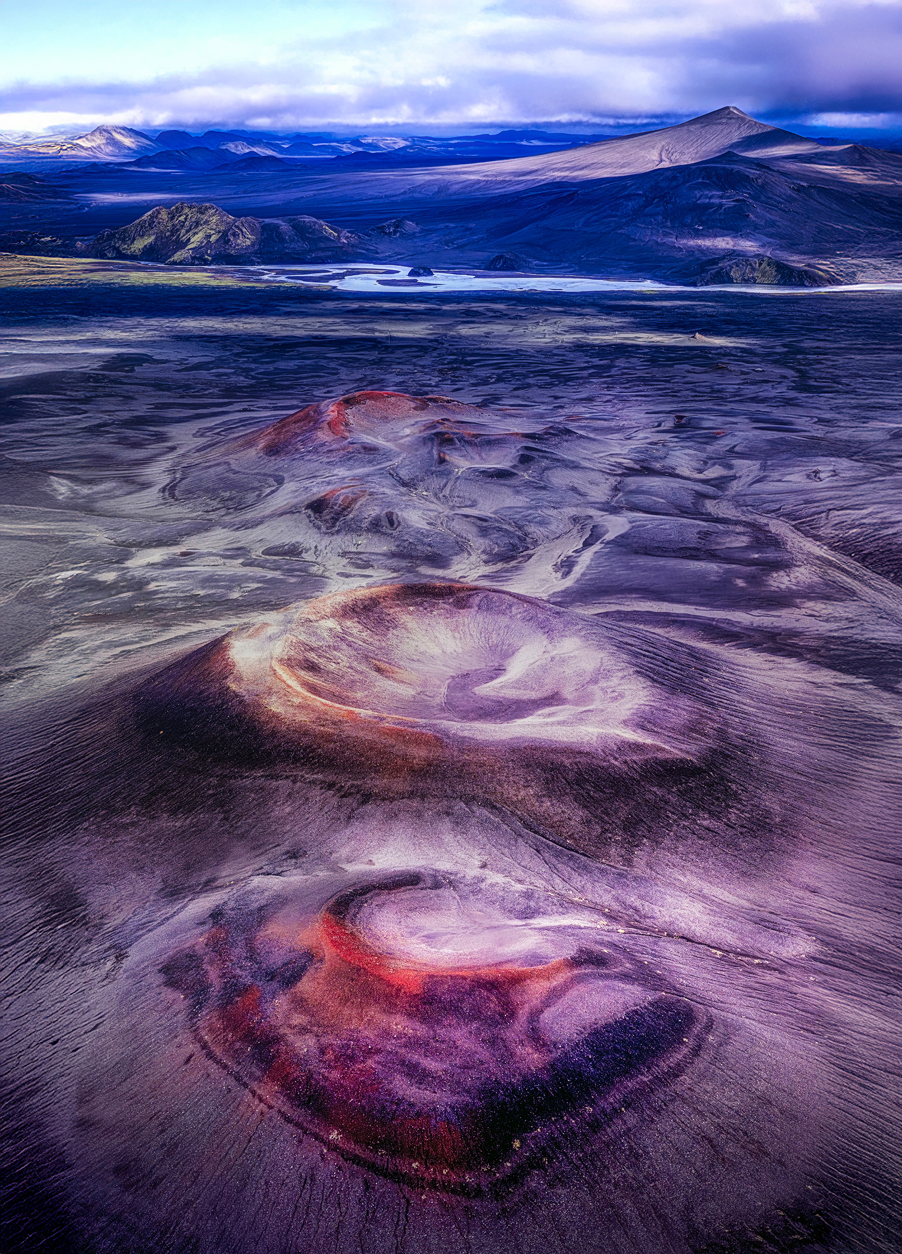 Aerial view of three volcanic craters rimmed in red and violet across black sand in the Fjallabak Highlands of Iceland