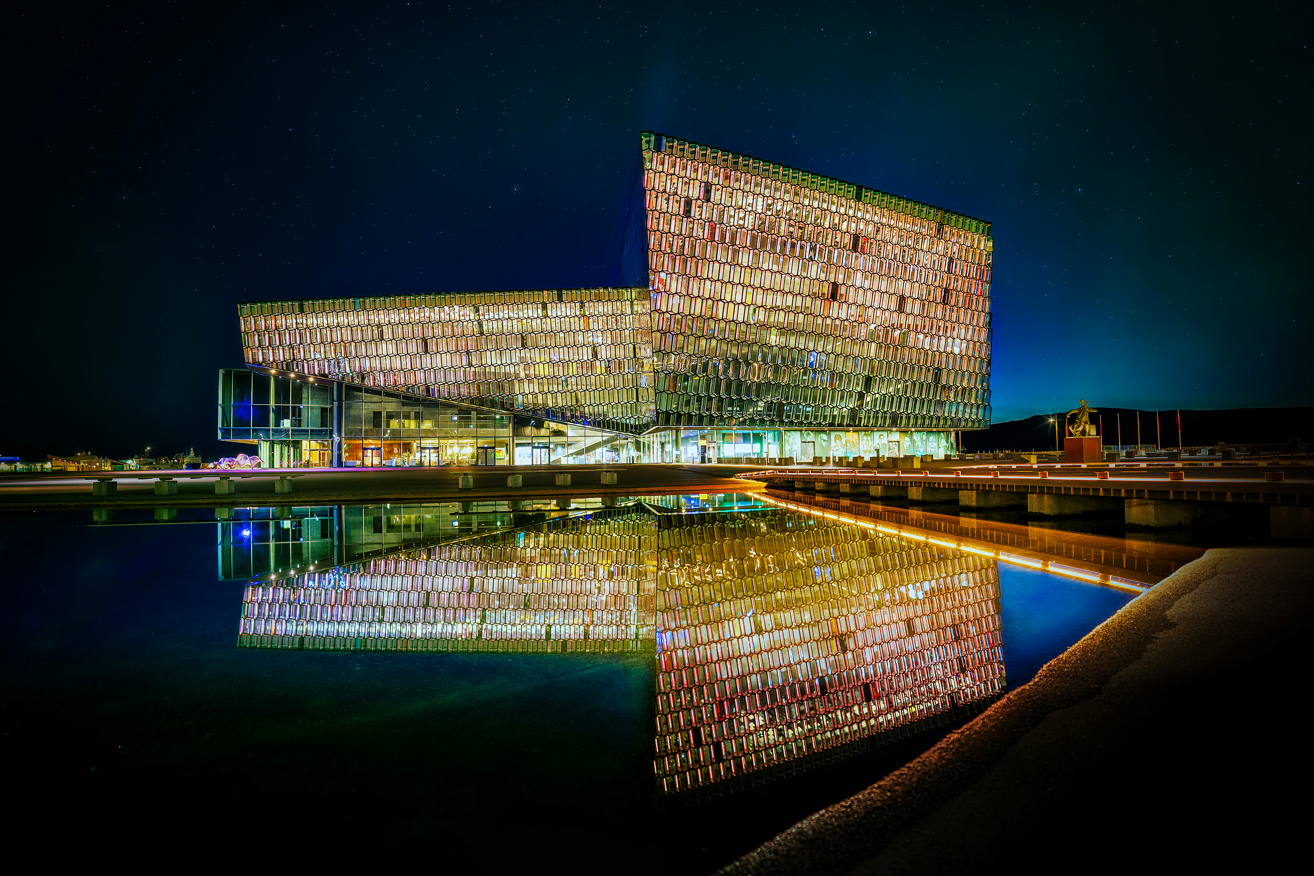 Harpa concert hall glowing at night in Reykjavik, its glass facade mirrored in still water