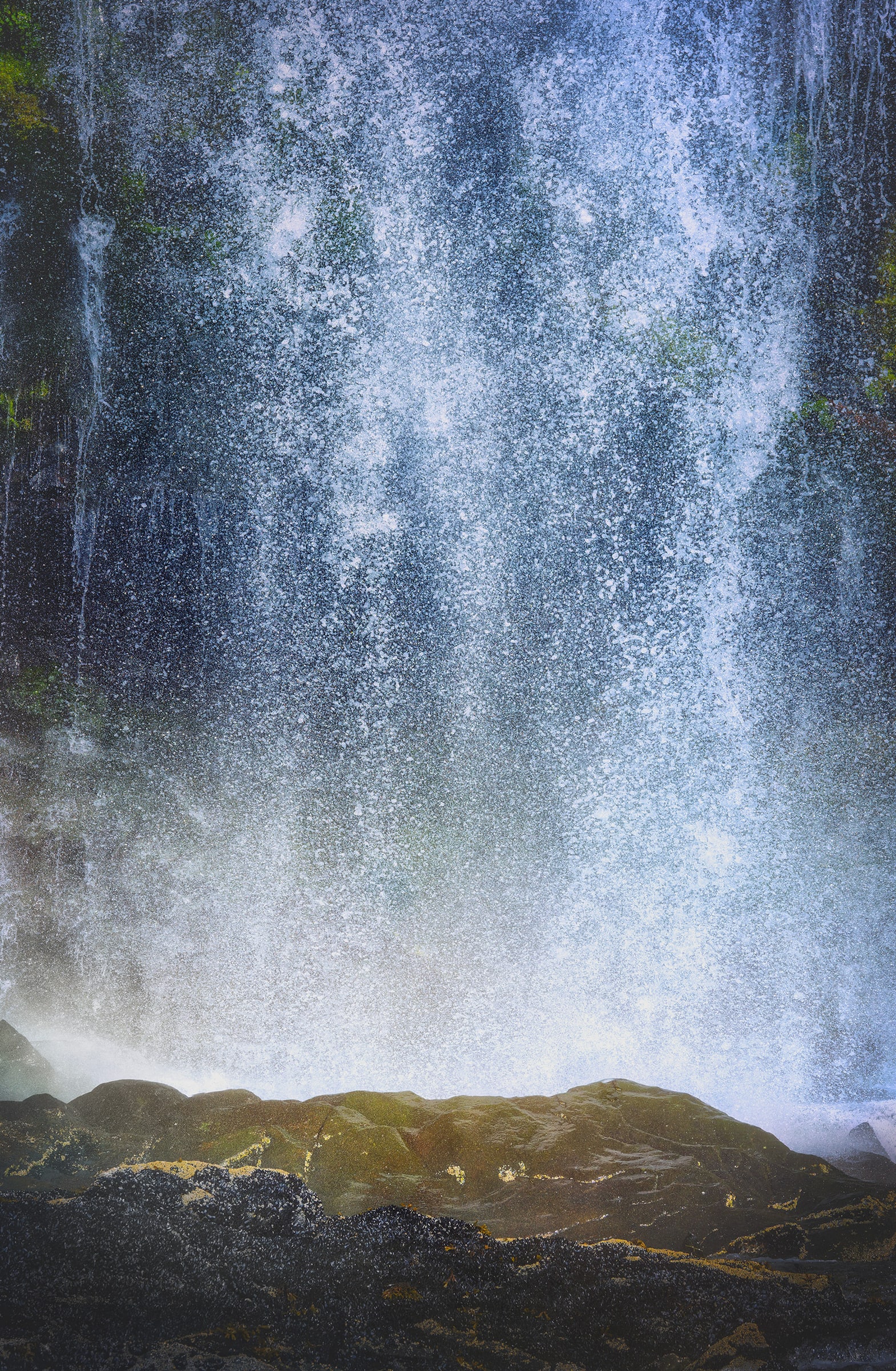 Fine art photograph of a powerful waterfall crashing over dark moss-covered rocks in Prince William Sound, Alaska, photographed from a boat in the morning, with cascading water and suspended spray creating an almost abstract view of the Alaskan wilderness.