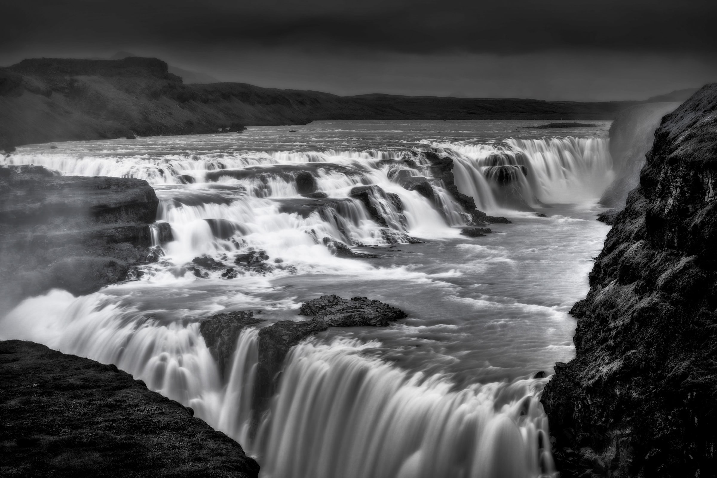Black and white fine art photograph of Gullfoss Waterfall, Iceland, with luminous silver cascades flowing over dark volcanic rock beneath a moody sky.